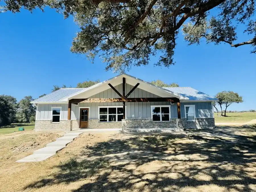Front view of a single-story ranch-style house with board-and-batten siding, stone skirting, and an exposed timber truss on the porch