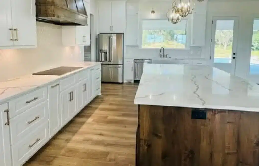 A modern, white kitchen with clean lines and sleek finishes, featuring a large central island, light wood flooring, stainless steel appliances, and stylish pendant lighting.